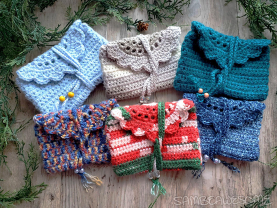 Photo of different handmade crochet pouches with a semi-circle scalloped edge flap, and a yarn chain wrap to close them, with beads on the end of the chain. Each is a different color and in all sorts of color ways, all winter (with one Christmas) themed.