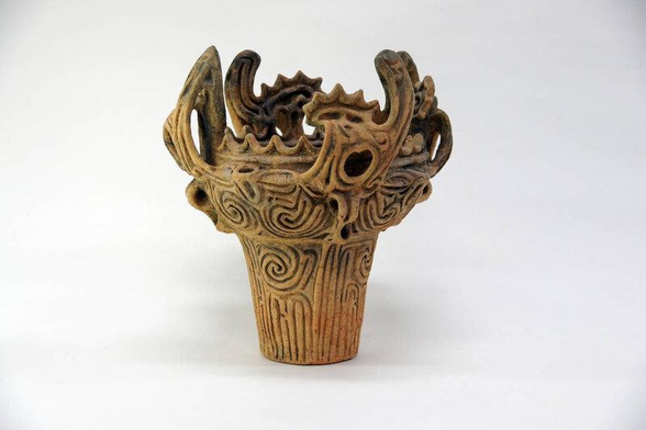 a cup for holding liquids with swirling designs inscribed on it, and flame-like elements done in stone to the cup , coming up and outwards from the top half of it 