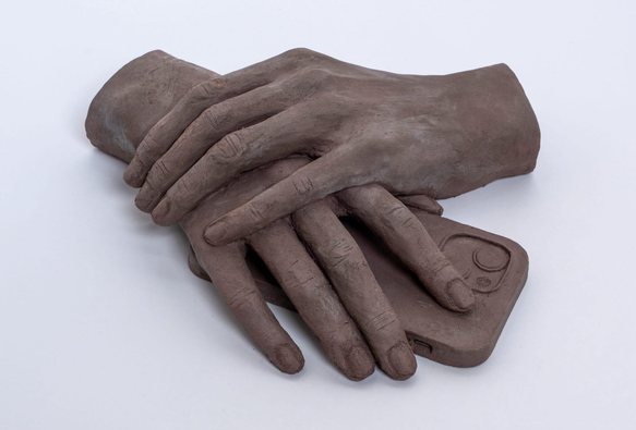 a clay sculpture by Léonore Chastagner of two hands folded over a smartphone