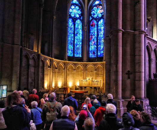 A group of about 20 people looking up at a stained glass window in a Gothic cathedral