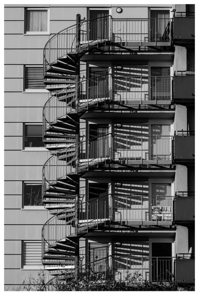 A spiral staircase on the facade of a house is illuminated by the sun in such a way that the shadow of the staircase is a perfect reflection.