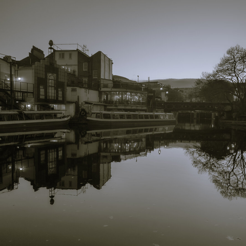 Monochrome mobile shot of buildings, canal boat, and bridge on Regent's Canal reflected in the water at Camden Town, London
Captured by Komeil Karimi