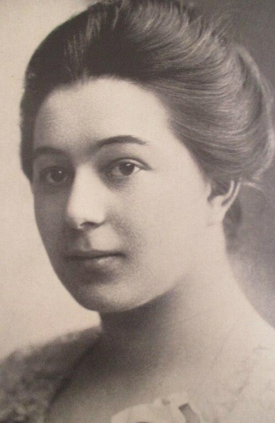 a photograph of the artist, her hair tied up, seen from her upper chest up, wearing a dress, looking to the left of the viewer, she has a calm expression on her graceful face 