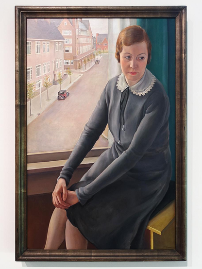 Schilderij van een oudere vrouw, keurig gekleed in een grijze jurk met een kanten boordje zit voor het raam waar je heel duidelijk de lege straat ziet door het hoge standpunt. Dat laatste is een kenmerk van de kunststroming de 'Nieuwe Zakelijkheid'.