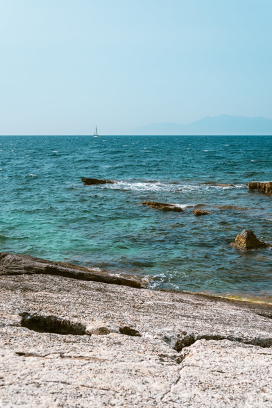 A photo of a bay with rocky beaches. There is a boat in the background. The sky is cloudless.