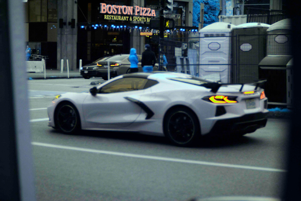 An out-of-focus supercar at a stop light, in a grey-looking urban environment with blue trees.