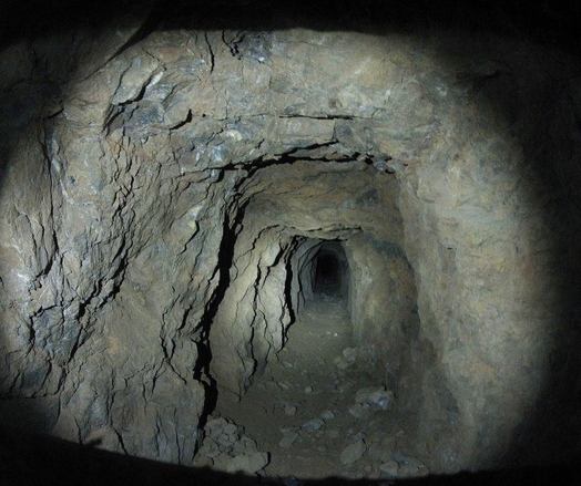 A flashlight-lit mine tunnel carved through the rock.