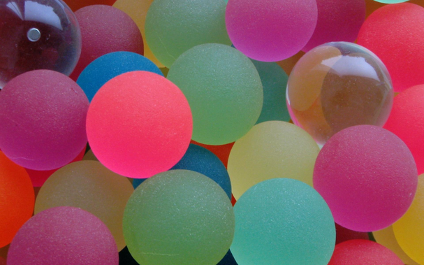 A closeup of a collection of multi-colored mostly translucent bouncy balls with differing textures.