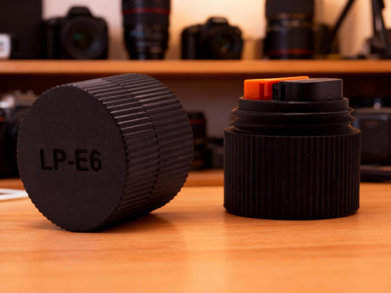 AI generated photo showing two views of the Canon LP-E6 size battery storage container on a table with camera equipment in the background.