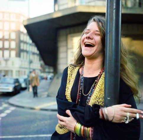 Janis Joplin hilare dans la rue, se tenant à un réverbère