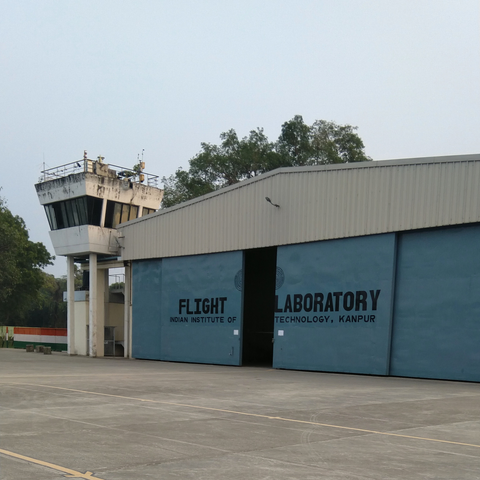 Flight hangar at IIT Kanpur with a control tower and large doors. Trees and clear sky in the background