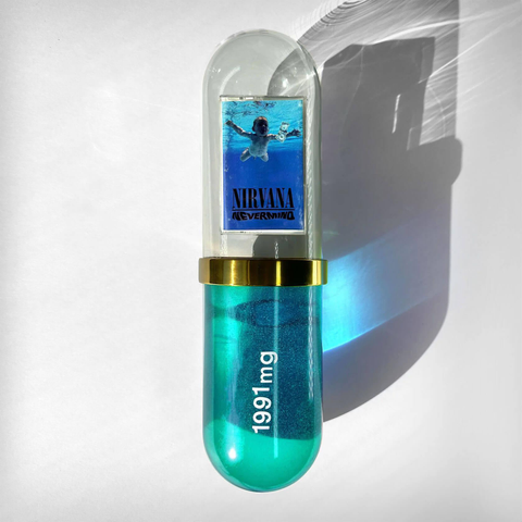 A capsule-shaped object features Nirvana's "Nevermind" album cover and blue glittery contents labeled "1991 mg."