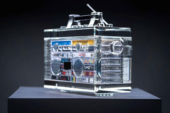 A clear acrylic boombox featuring colorful cassette tapes and detailed speaker designs, displayed against a dark background.