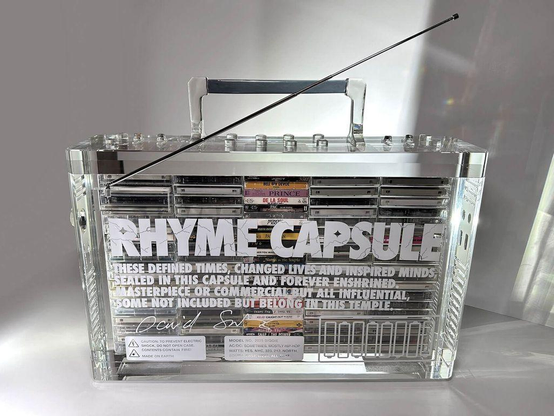 A transparent boombox display titled "Rhyme Capsule," featuring various audio cassettes inside and a message about influential music.