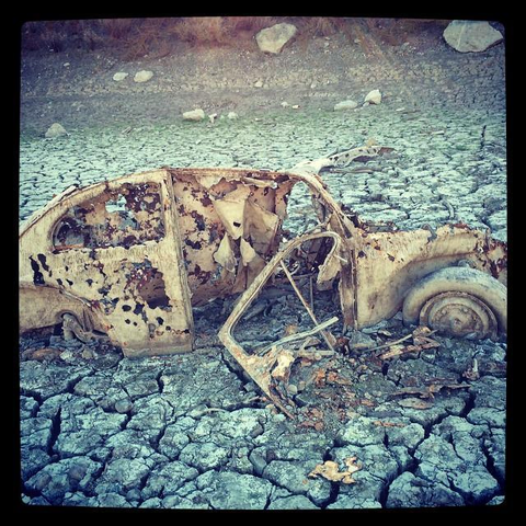 A rusted out and shot-up old car remnant sits on a dried reservoir bed.