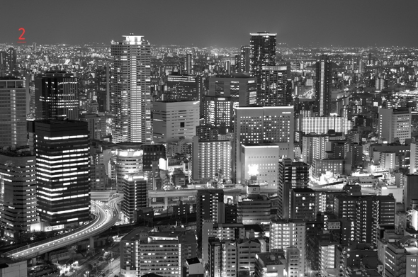 Photo noir et blanc de nuit d'une vue de la ville d'Osaka depuis le toit terrasse d'une tour. On voit de nombreuses tours ainsi que des voies aériennes jusque dans le lointain.