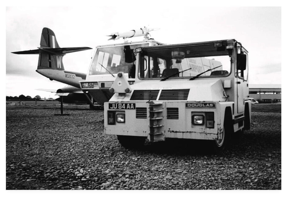Black and white photograph of vintage airfield vehicles at Carlisle Aviation Museum.  To the left a jet, in the middle a fire tender, and to the right an aircraft tug.