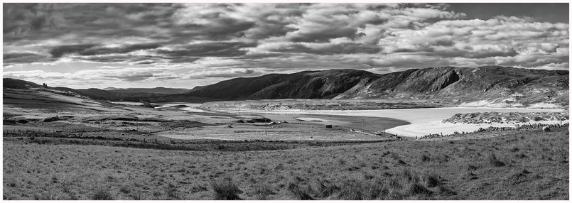 A panoramic black-and-white landscape of rolling hills and a winding river. The scene features a mix of grassy fields, rocky hills, and scattered clouds in the sky.
