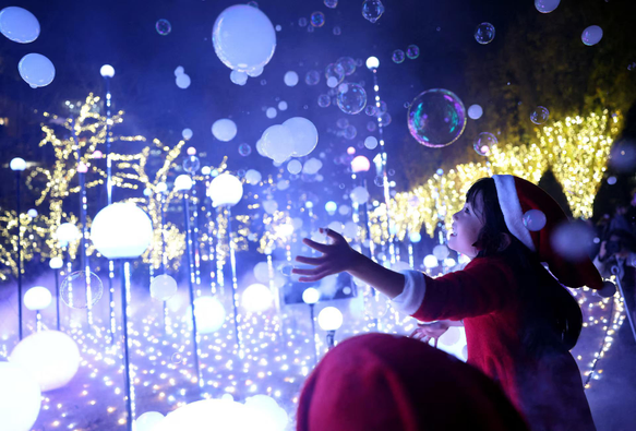 A 6-year-old girl wearing a Santa Claus costume tries to catch soap bubbles in the air at an illumination event celebrating the upcoming the Christmas season at a park.