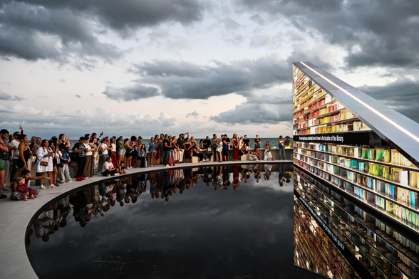 People look at an installation by the British artist Es Devlin. Library of Us is a 15-metre-long (50ft) rotating triangular bookshelf containing 2,500 books that have shaped the artist’s life, set in a pool.