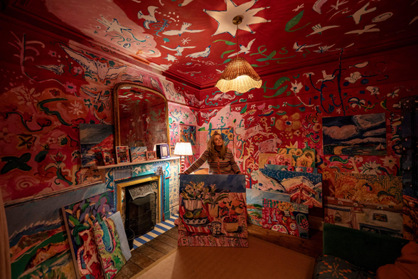 The artist Emily Powell inside the living room of her terraced home with paintings covering all surfaces.