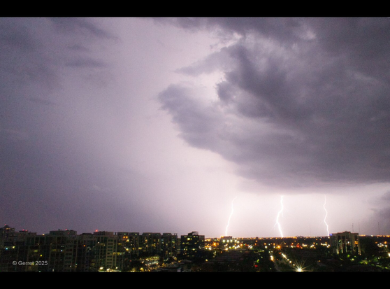Dramatic night scene with dark storm clouds over a city skyline. Three bright lightning strikes illuminate the horizon, reflecting an intense, electrifying atmosphere.
