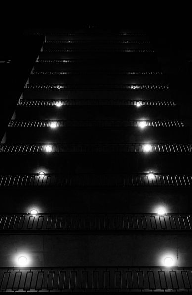 The black-and-white photo shows a high-rise building (view from bottom to top) with many illuminated balconies, which creates a resemblance to an airstrip.