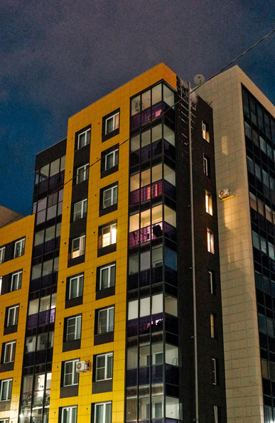 Late evening. Dark blue sky. Close-up of an orange high-rise with illuminated windows.