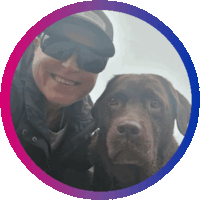 Round animated avatar image. It's a selfie of Arwen, a chocolate brown Labrador, and Cynni, a person smiling and wearing a cap and sunglasses. The image zooms in on Arwen's snout. The circle has a border in the colors if the bisexuality flag.