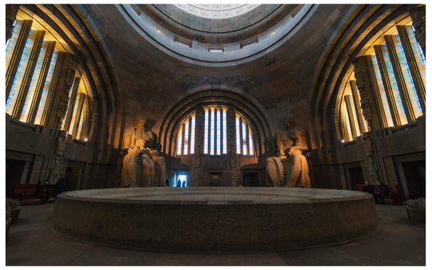 Blick in eine Herr-der-Ringe-Style Halle mit riesigen Statuen, Fenstern und einer Kuppel. 