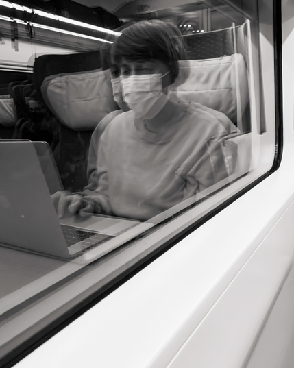 Ich schaue und fotografiere aus einem Zugfenster heraus. Dabei spiegelt sich die mir gegenüber sitzende Frau im Zugfenster so deutlich, dass man meint die Aufnahme wäre von draussen gemacht worden. Das Foto ist in Schwarzweiß.