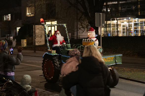 A small green tractor with a person clothed like Santa behind the steering wheel. 