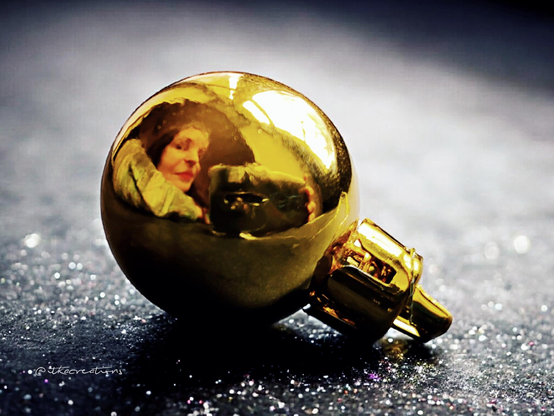 Une boule de noël posée sur un comptoir gris parsemé de Paillettes. Dans le reflet on aperçoit mon visage.
