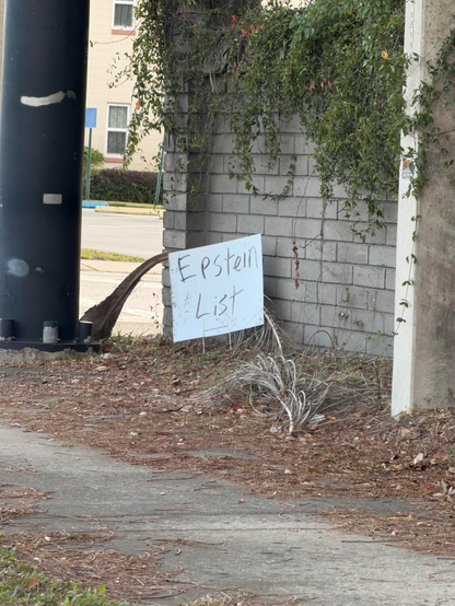A handwritten yard sign that reads “Epstein List” seen at a red light.