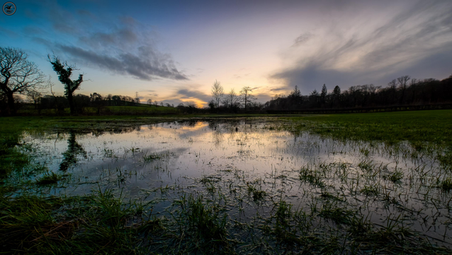 Landscape shots over water soaked wet field with sunset over far trees