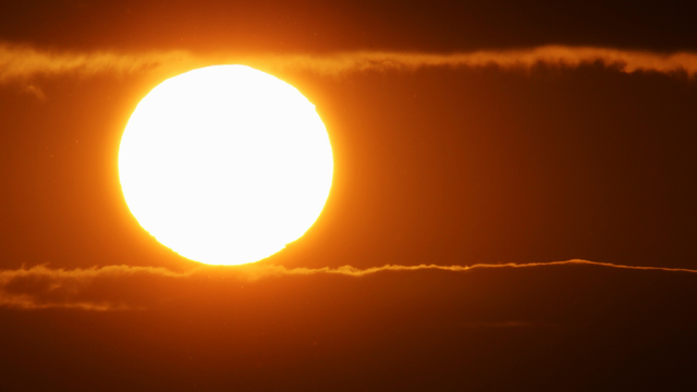 Photograph of a large white sun between two parallel horizontal yellow lines formed by the boundaries of clouds just above and below, each tangental to the top and bottom of the sphere of the sun.