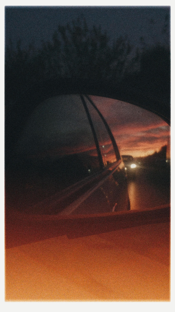 A photo from the front seat of car capturing the amazing sunset that is behind in the front mirror.