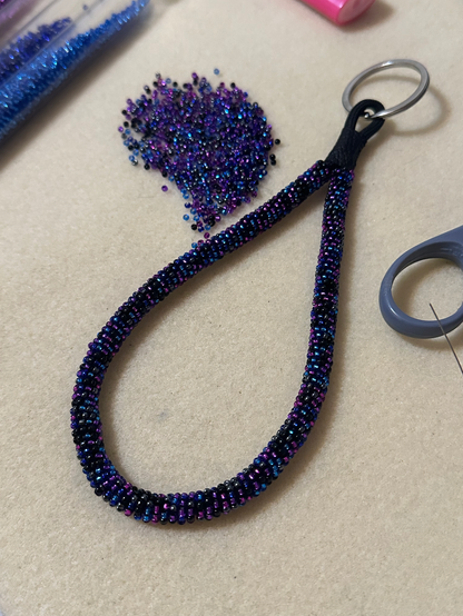 A bead wrapped keychain in black, blue, and purple
