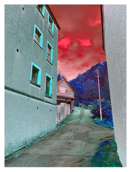 Colour adjusted portrait photograph showing a path leading up beyond two apartment blocks.  The sky is red and the trees in the distance are blue.