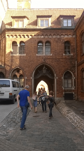 Photo to the entrance of the Doma Cathedral inner square, with the gates open, with a bunch of people going in and coming out.
