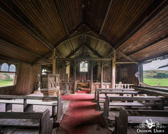 A photo features the interior of an abandoned wooden church. Pews line a red carpet towards the altar and pulpit