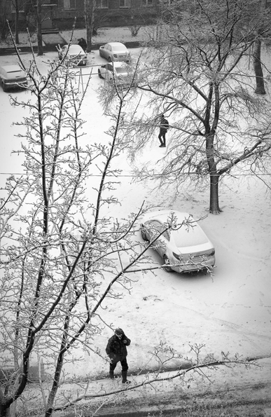 The black-and-white photo shows the courtyard (top view) between the houses after the last snowfall.  Trees, a car, and two people walking are visible.