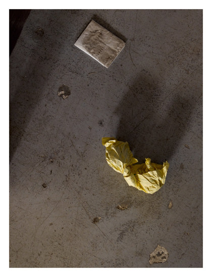 A scuffed floor with a trash of a yellow paper and a napkin.