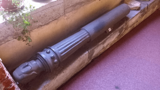 Photo of an old cannon (maybe????), placed on an edge of stone wall, low to the ground, right by the windows.