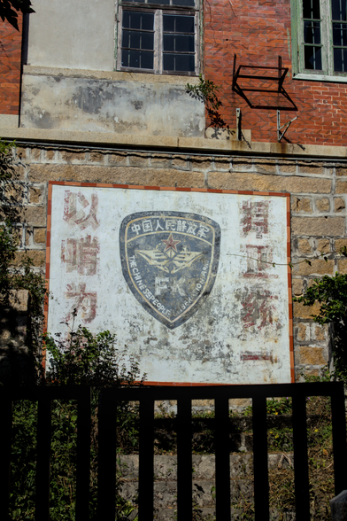 some kind of faded mural on a red brick wall with chinese text and a police shield in the middle