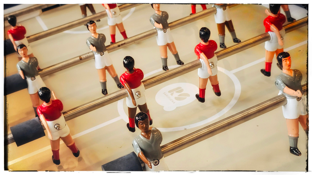A picture of a tabletop foosball game. Rows of ceramic soccer players, screwed to metal rods, stand at the ready, waiting for someone to toss a soccer ball onto the table. While they are hanging there, waiting, the players have their right arm extended straight out. It appears they are all practicing passing something to an infantile president... something FIFA actually does.