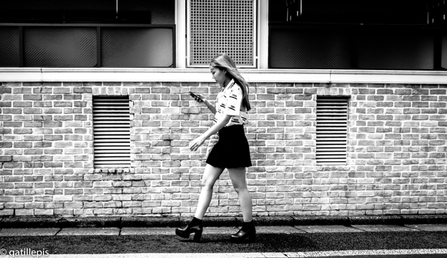 Noia amb faldilla curta, sabates amb tacó caminant mentre mira el mòbil.