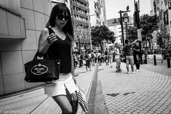 Dona amb cabells llargs, ulleres de sol, bossa de marca i faldilla curta sortint d'uns grans magatzems.