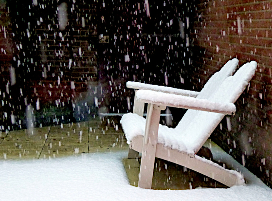 Foto van tuinbankje bedekt met sneeuw en vallende vlokken