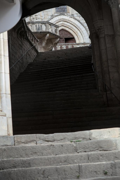 Des escaliers en pierre qui montent. On aperçoit une porte de chapelle au sommet